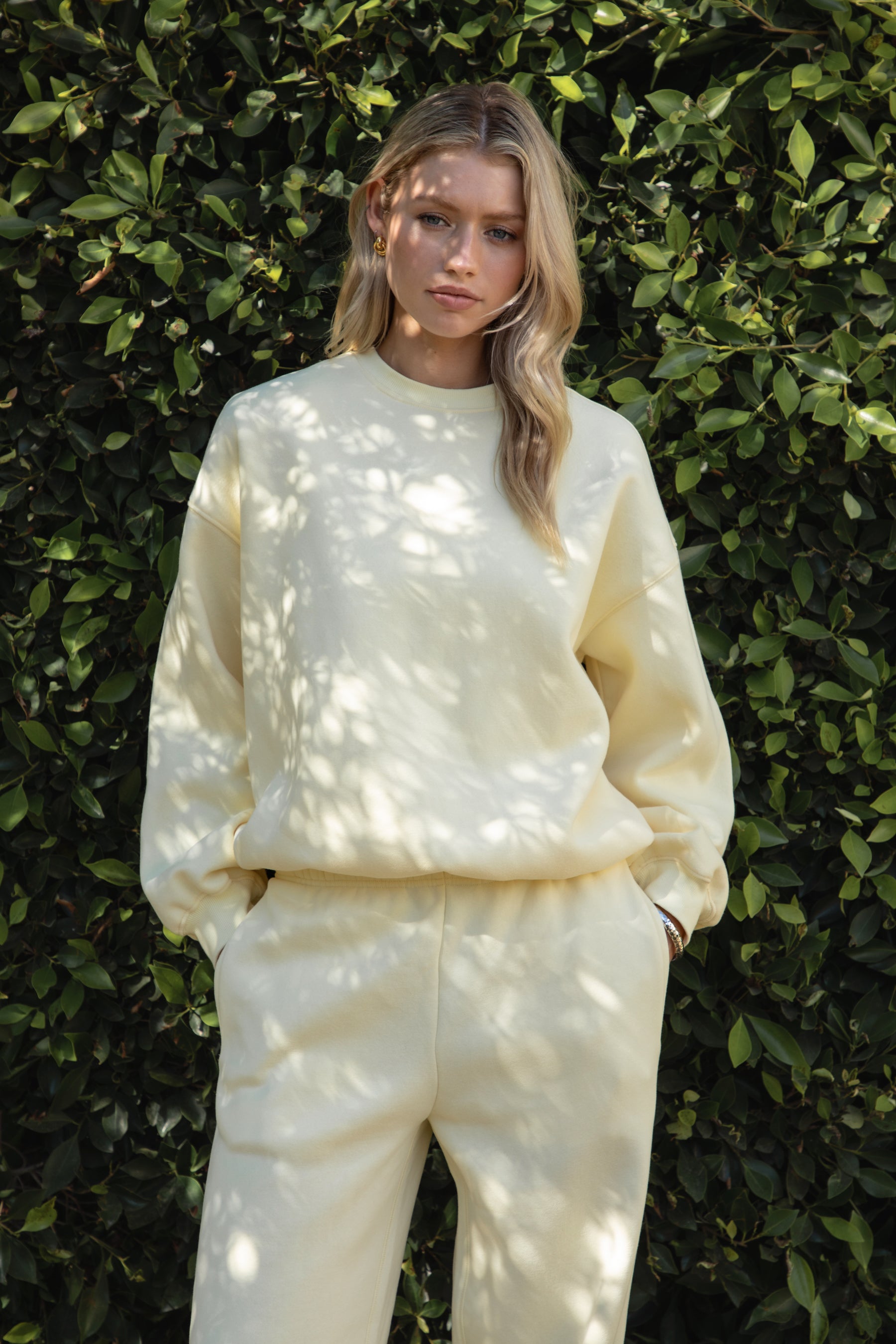 Woman wearing a yellow colored outfit standing against a green leafy background