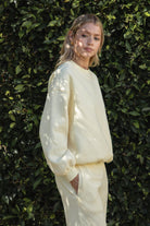 Woman wearing a yellow colored outfit standing against a green leafy background