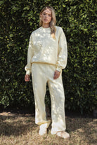 Woman wearing a yellow colored outfit standing against a green leafy background