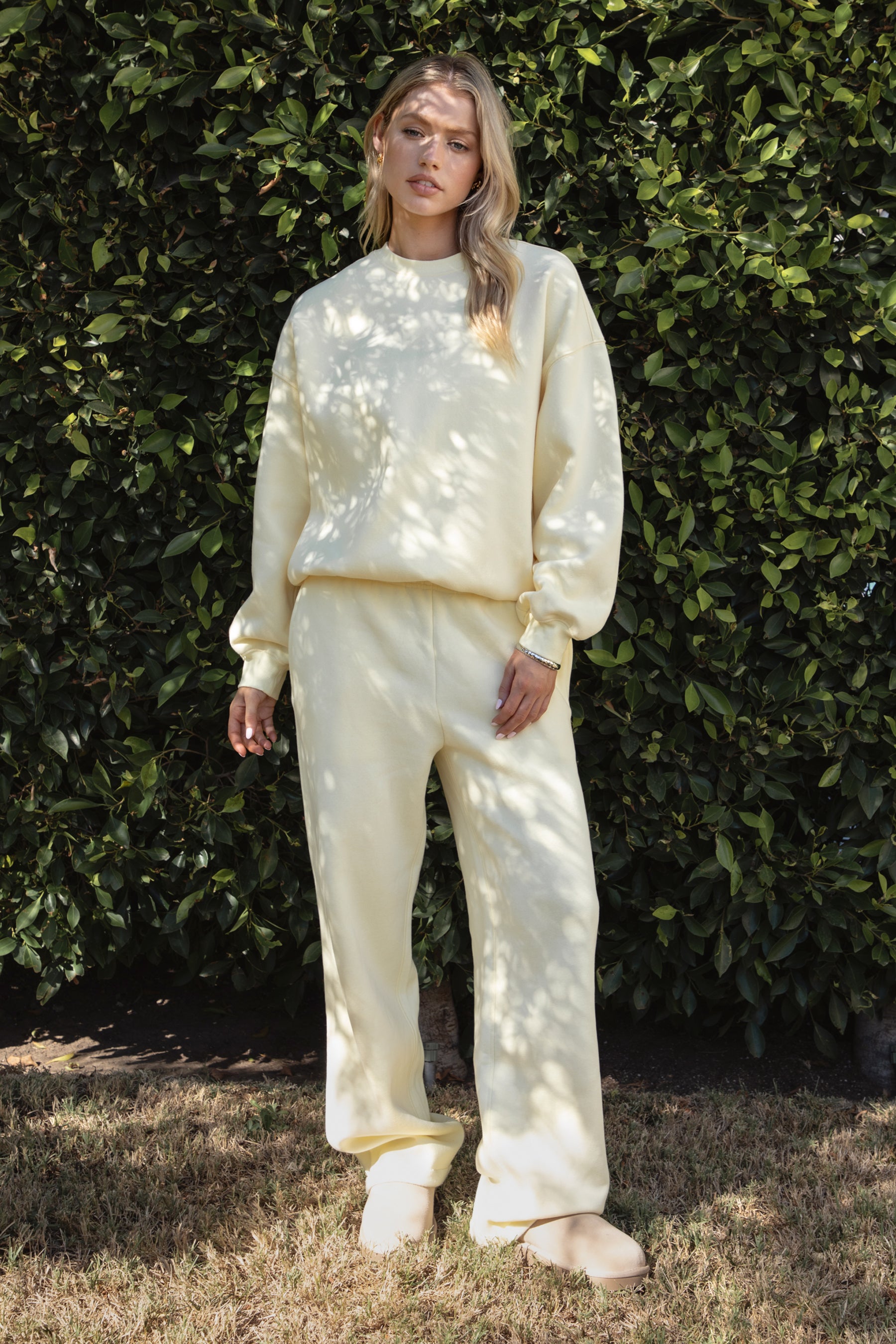 Woman wearing a yellow colored outfit standing against a green leafy background