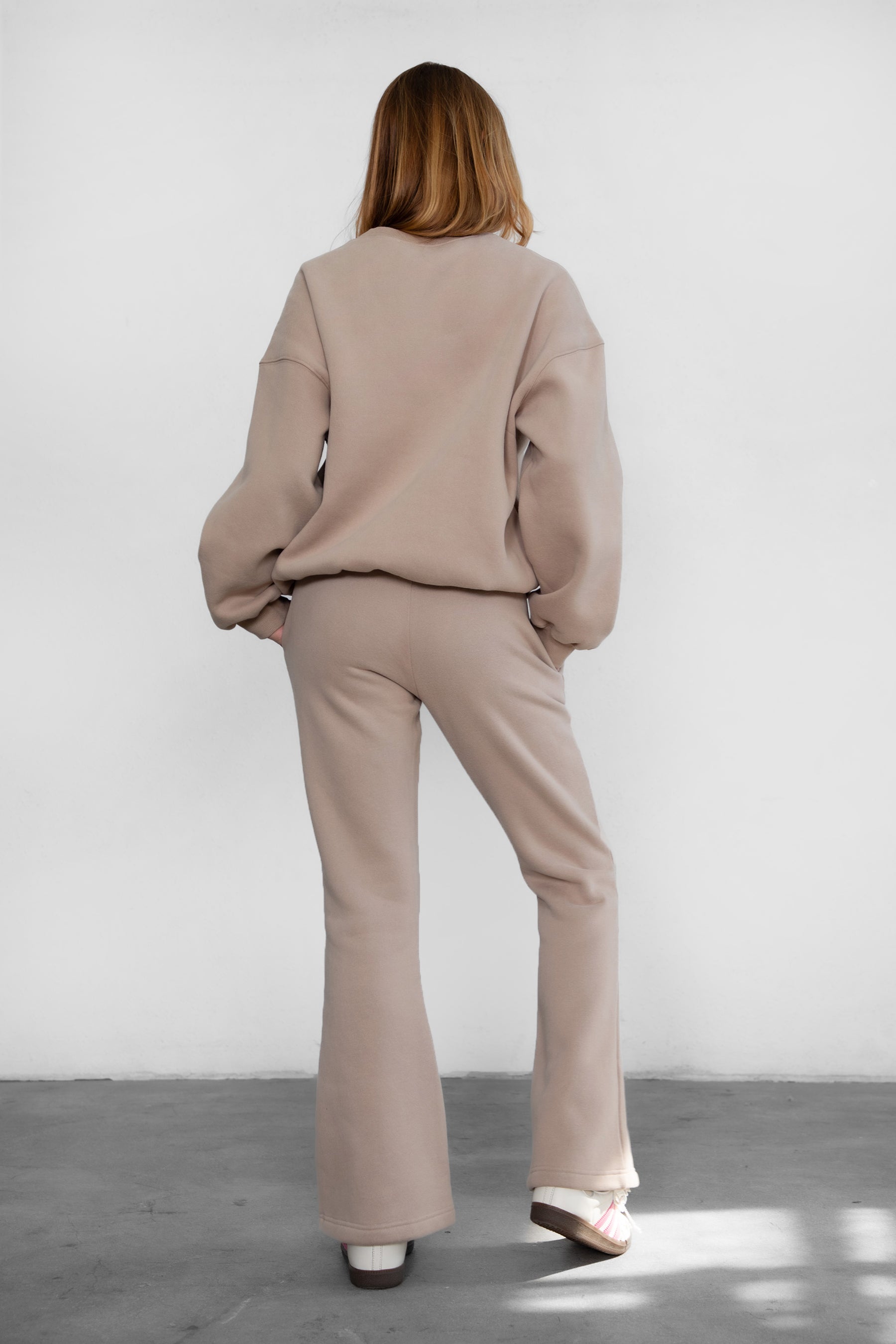 Person wearing a beige outfit standing against a white wall.