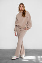 Woman wearing a beige tracksuit with white sneakers on a light gray floor and white background