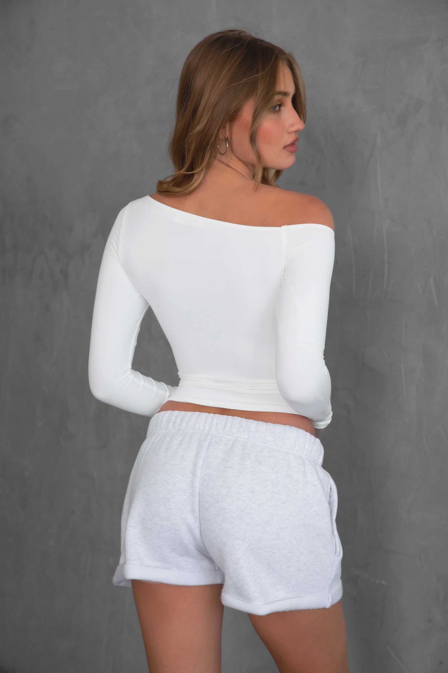 Woman wearing TIC TOC TH30538 AUDREE lightweight one-shoulder long sleeve top in slim fit stretch fabric in color white paired with fleece shorts. 