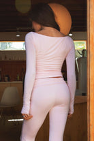 Woman wearing the TIC TOC TH30643 JOLINA blush core basic long sleeve top featuring high boat neckline, thumbhole sleeves, and ruched detailing along the bodice with matching bottoms in an indoor setting.