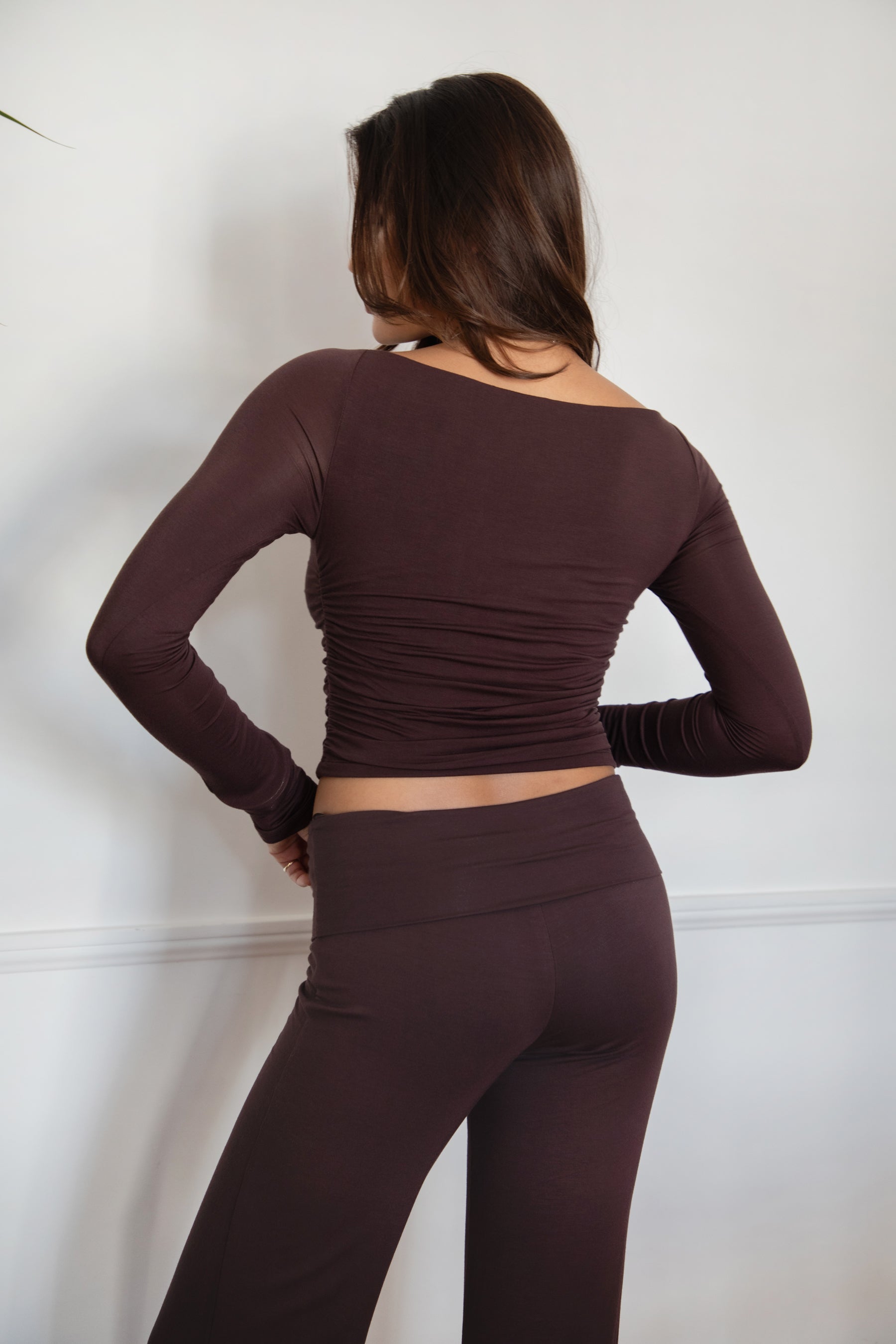 Woman wearing the TIC TOC TH30643 JOLINA brown core basic long sleeve top featuring high boat neckline, and ruched detailing along the bodice with matching bottoms in an indoor setting.