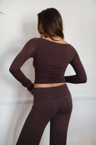 Woman wearing the TIC TOC TH30643 JOLINA brown core basic long sleeve top featuring high boat neckline, and ruched detailing along the bodice with matching bottoms in an indoor setting.