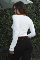 Model wearing TIC TOC TH31573BA RAYAE asymmetric off-the-shoulder jersey top with wide neckline and draped long sleeves paired with polka dot black capri pants in an outdoor setting. 