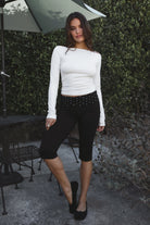 Model wearing TIC TOC TH31573BA RAYAE asymmetric off-the-shoulder jersey top with wide neckline and draped long sleeves paired with polka dot black capri pants in an outdoor setting. 