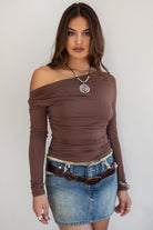Woman wearing the TIC TOC TH31664 VELARI brown cowl neck long sleeve top featuring a draped neckline, off-the-shoulder fit, and side ruching detail paired with a denim mini skirt