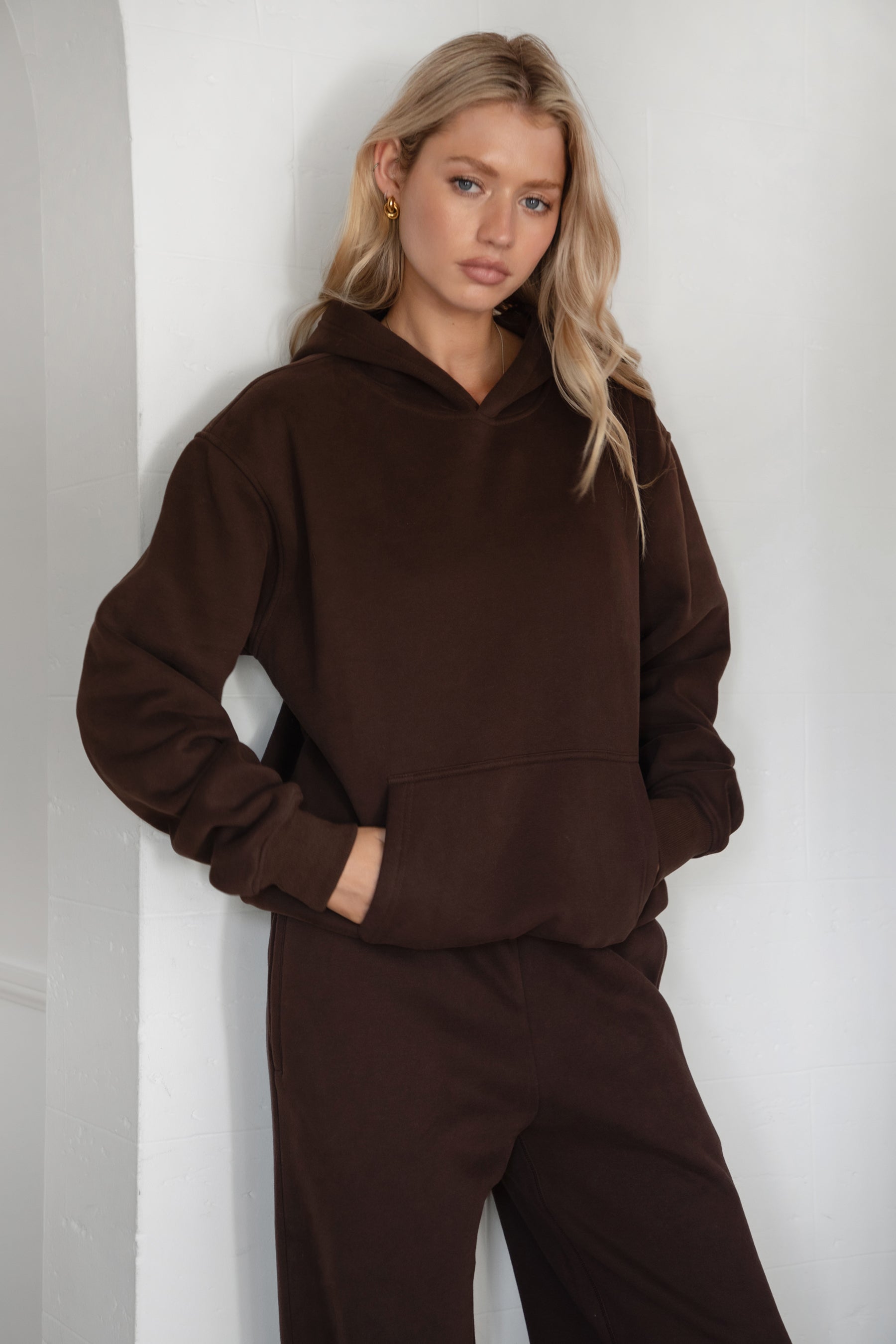 Woman wearing the TIC TOC TJ31007 DAMI dark brown cloud fleece oversized hoodie featuring a dropped shoulder design, kangaroo pocket, and ribbed cuffs with matching bottoms.