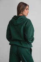 Woman wearing the TIC TOC TJ31007 DAMI forrest green cloud fleece oversized hoodie featuring a dropped shoulder design, kangaroo pocket, and ribbed cuffs with matching bottoms.