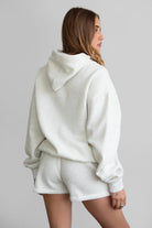 Woman wearing the TIC TOC TJ31007 DAMI heather white cloud fleece oversized hoodie featuring a dropped shoulder design, kangaroo pocket, and ribbed cuffs with matching bottoms.
