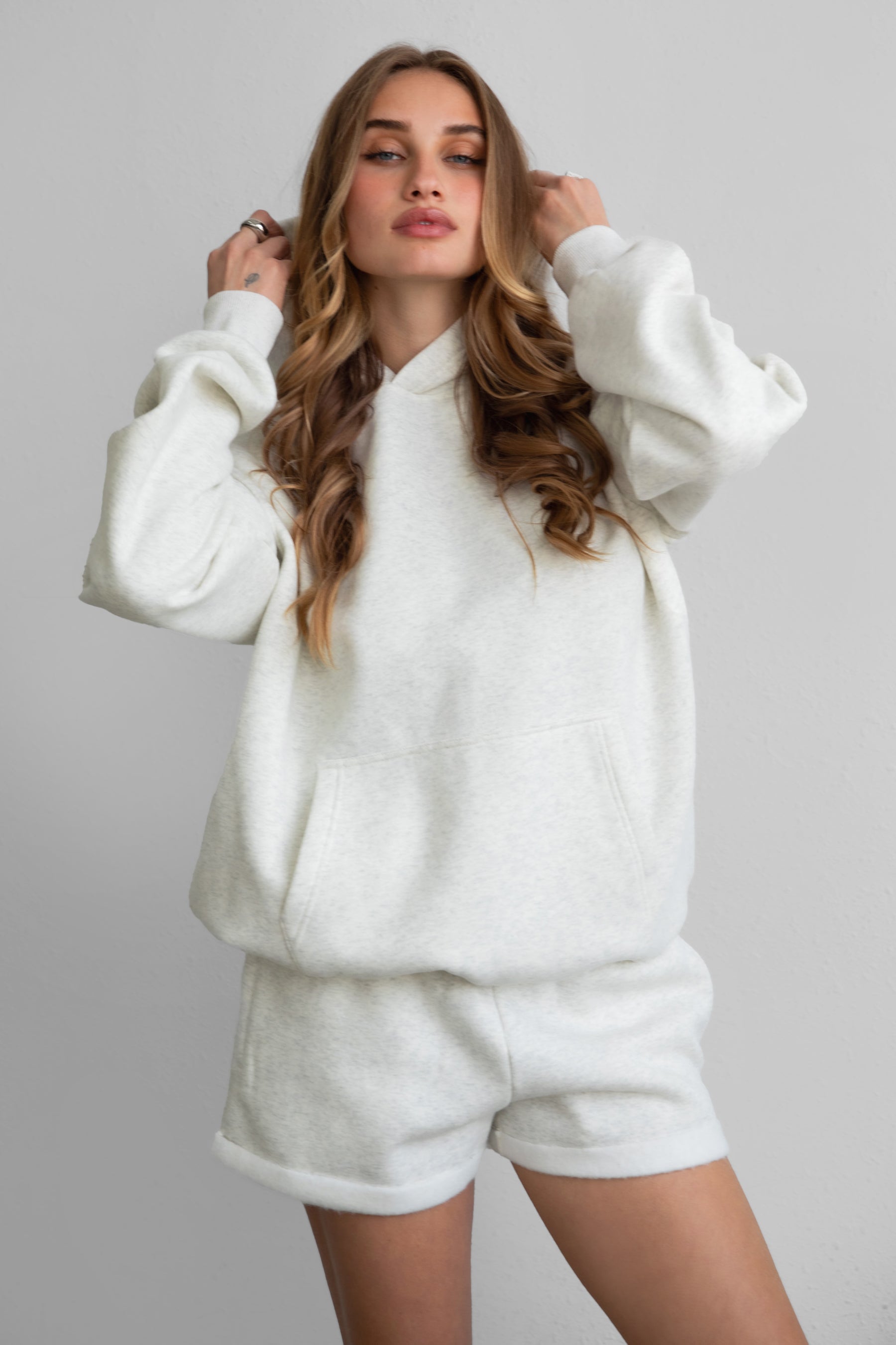 Woman wearing the TIC TOC TJ31007 DAMI heather white cloud fleece oversized hoodie featuring a dropped shoulder design, kangaroo pocket, and ribbed cuffs with matching bottoms.