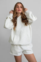 Woman wearing the TIC TOC TJ31007 DAMI heather white cloud fleece oversized hoodie featuring a dropped shoulder design, kangaroo pocket, and ribbed cuffs with matching bottoms.