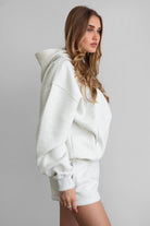 Woman wearing the TIC TOC TJ31007 DAMI heather white cloud fleece oversized hoodie featuring a dropped shoulder design, kangaroo pocket, and ribbed cuffs with matching bottoms.