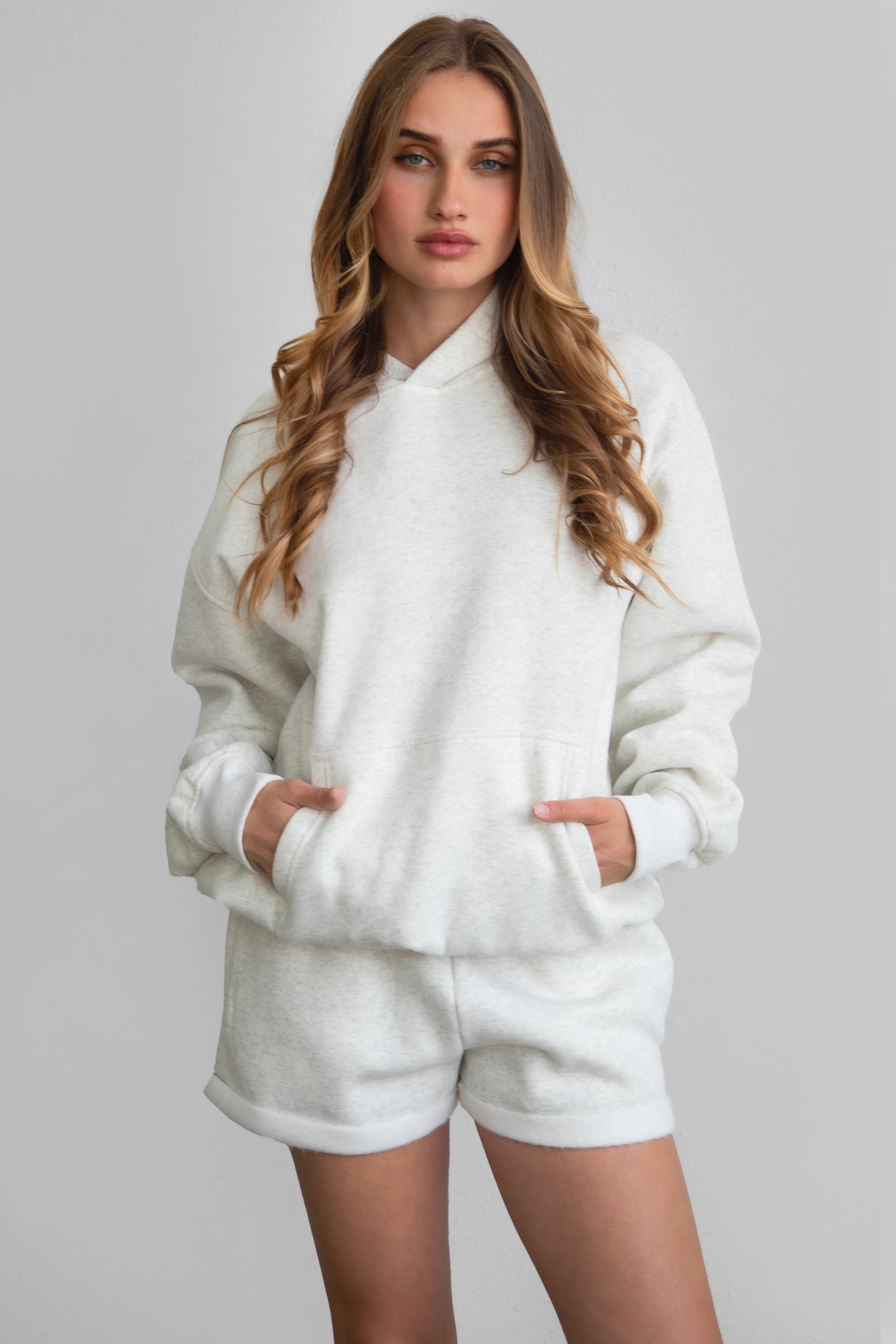 Woman wearing the TIC TOC TJ31007 DAMI heather white cloud fleece oversized hoodie featuring a dropped shoulder design, kangaroo pocket, and ribbed cuffs with matching bottoms.