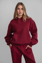 Woman wearing the TIC TOC TJ31007 DAMI maroon cloud fleece oversized hoodie featuring a dropped shoulder design, kangaroo pocket, and ribbed cuffs with matching bottoms.