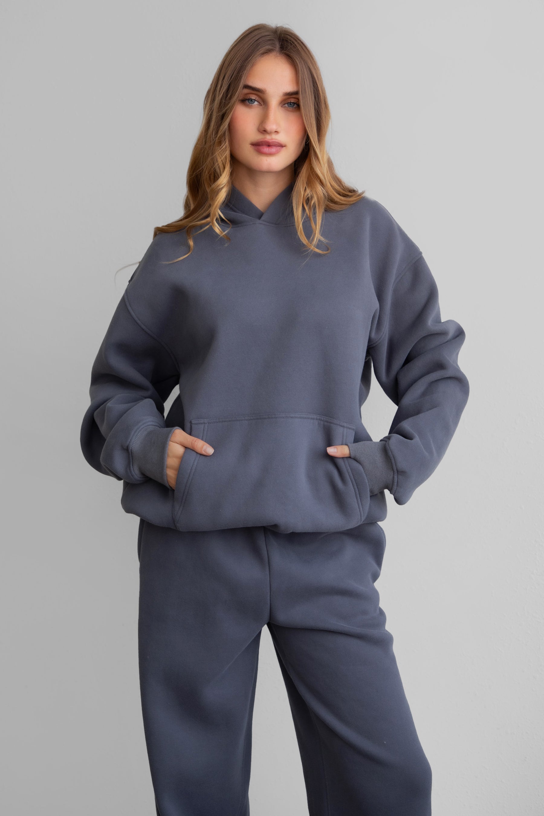 Woman wearing the TIC TOC TJ31007 DAMI steel grey cloud fleece oversized hoodie featuring a dropped shoulder design, kangaroo pocket, and ribbed cuffs with matching bottoms.