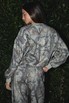 Woman wearing TIC TOC TJ31427 ELK woodland camo fleece crew neck sweatshirt with oversized fit, ribbed cuffs, and hem with matching bottoms against a dark background