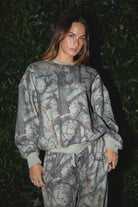 Woman wearing TIC TOC TJ31427 ELK woodland camo fleece crew neck sweatshirt with oversized fit, ribbed cuffs, and hem with matching bottoms against a dark background