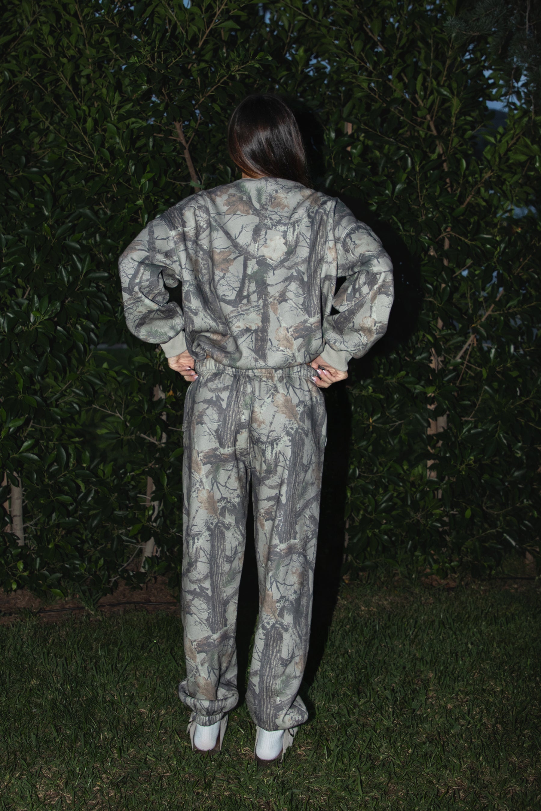 Woman wearing TIC TOC TJ31427 ELK woodland camo fleece crew neck sweatshirt with oversized fit, ribbed cuffs, and hem with matching bottoms against a dark background