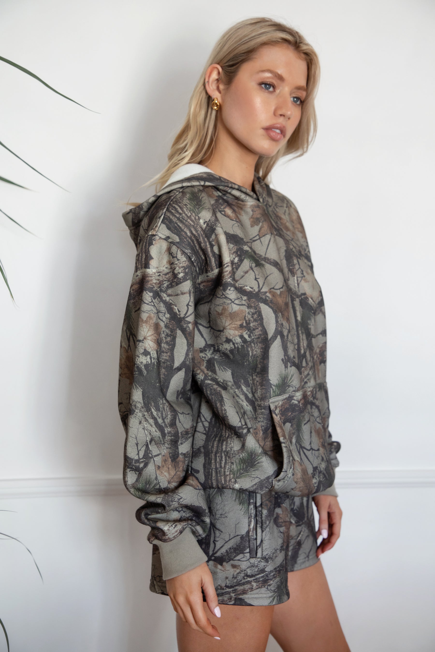 Woman wearing a camouflage hoodie and shorts against a white background
