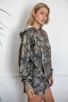 Woman wearing a camouflage hoodie and shorts against a white background
