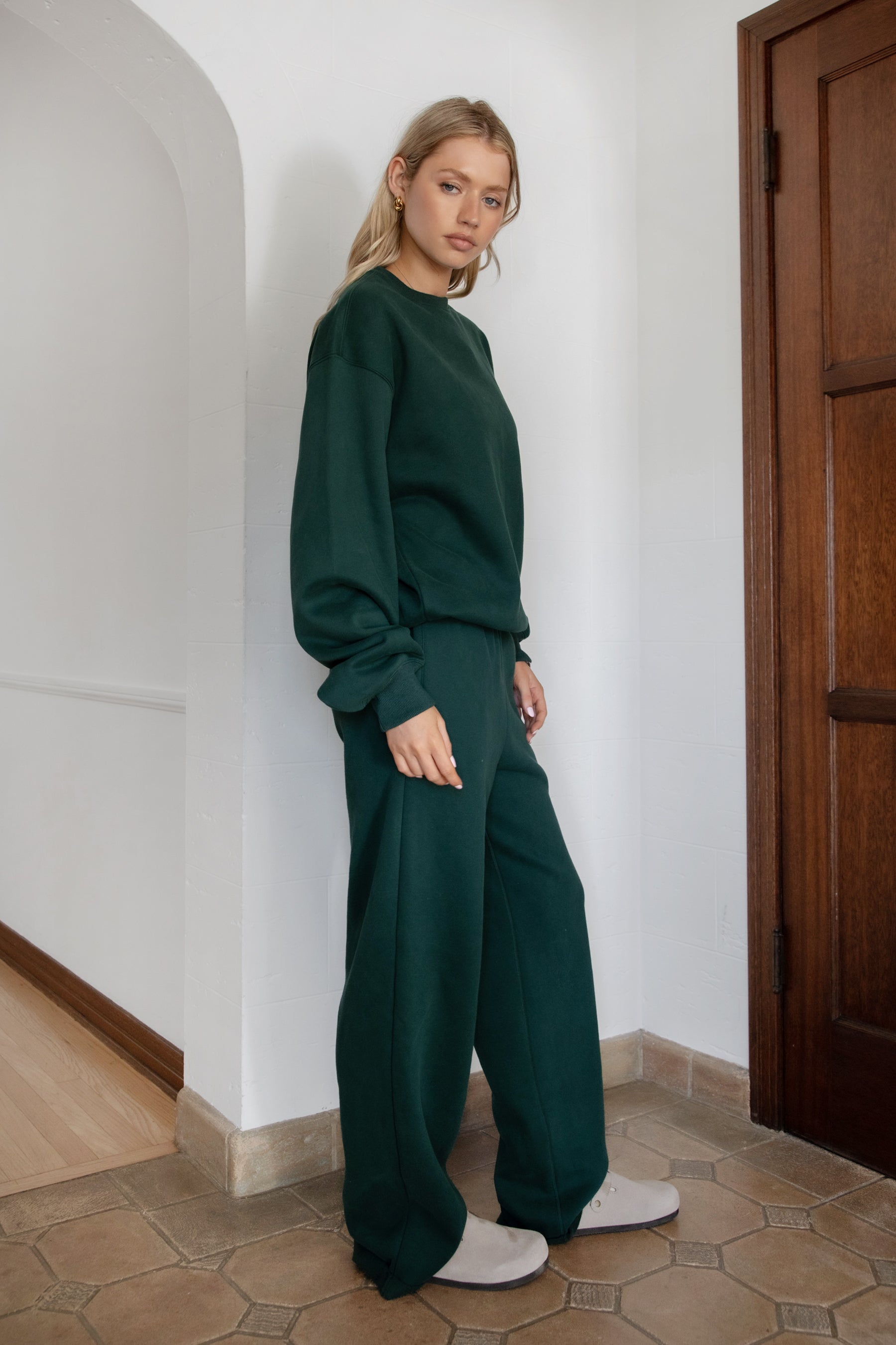 Woman wearing the TIC TOC TJ31656 LANI forrest green cloud fleece crew neck pullover sweatshirt featuring dropped shoulders, ribbed trim, and cozy fleece fabric with the matching bottoms .