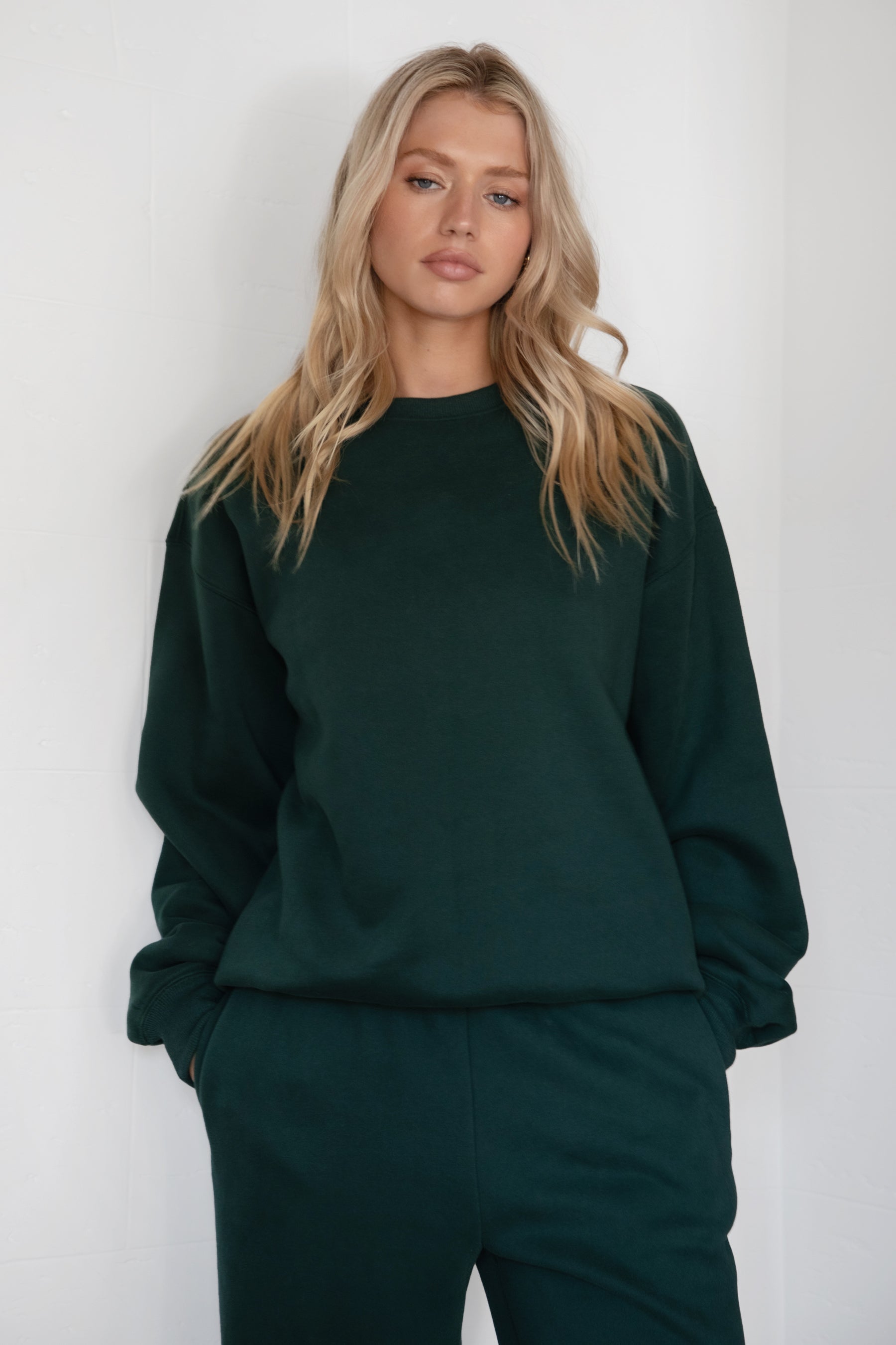 Woman wearing the TIC TOC TJ31656 LANI forrest green cloud fleece crew neck pullover sweatshirt featuring dropped shoulders, ribbed trim, and cozy fleece fabric with the matching bottoms .