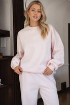 Woman wearing the TIC TOC TJ31656 LANI pale pink cloud fleece crew neck pullover sweatshirt featuring dropped shoulders, ribbed trim, and cozy fleece fabric with the matching bottoms indoors. 