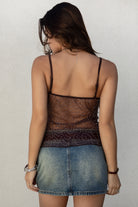 Woman wearing a beaded boho top and denim skirt against a plain background. 