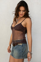 Woman wearing a beaded boho top and denim skirt against a plain background. 