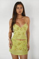 Model wearing the TIC TOC SL31480 VEDA brown chiffon beaded low-rise mini skort featuring hand-beaded floral embroidery, chiffon overlay, and built-in shorts with matching cami top in an outdoor setting. 