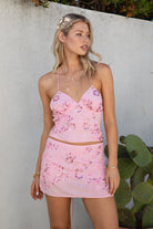 Model wearing the TIC TOC TL31430 VEDA pink chiffon beaded cami top featuring floral embroidery, plunging neckline, and lace-up open back with matching mini skirt in an outdoor setting