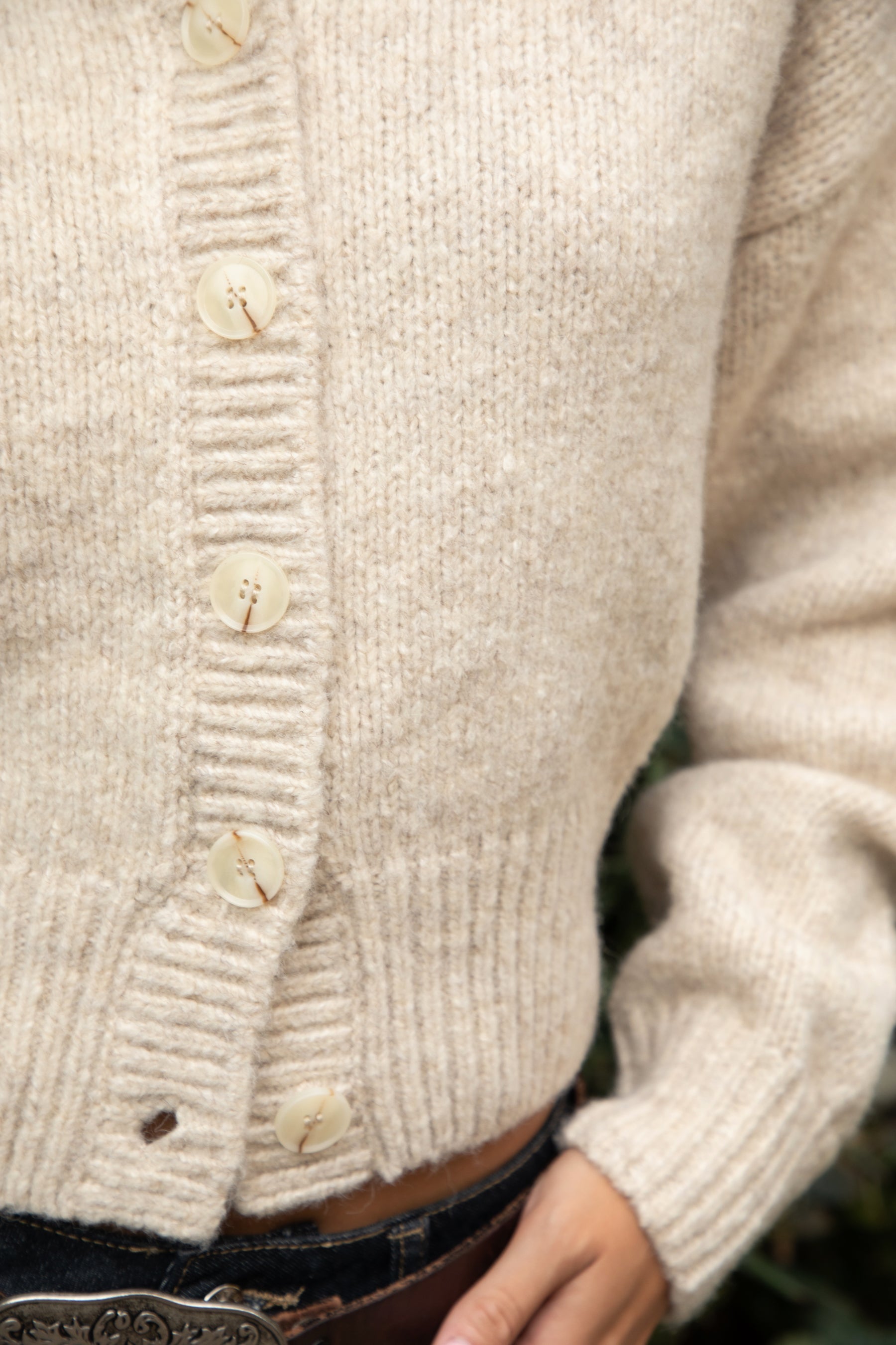 Close-up of a beige knitted cardigan with buttons on a blurred background