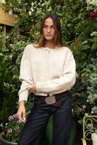 Woman wearing TIC TOC TV31637 MARLO oatmeal sweater knit button down cardigan with ribbed cuffs and dropped shoulders in cozy marled fabric paired with dark denim in a garden setting